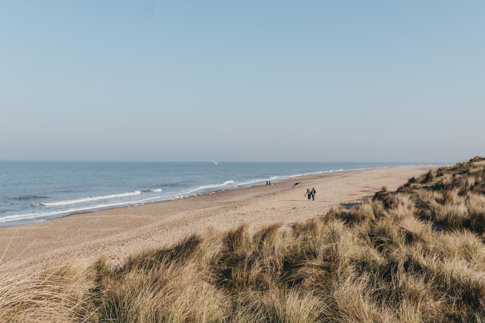 Hemsby, UK - April 19, 2019: Panoramic view from the hill over Hemsby beach on a sunny spring day, two people walking in the distance. Hemsby beach is a famous beach on the East Norfolk coast, UK.