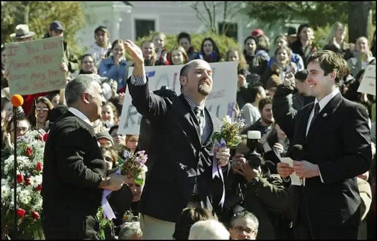 Village of New Paltz Mayor Jason West, right, stands by as Brook Garrett, center, blows a kiss to the audience after marrying Jay Blotcher, left, at the Village Hall in New Paltz on Friday, Feb. 27, 2004. West performed the ceremony. West was charged Tuesday, March 2, 2004 with 19 criminal counts for performing marriage ceremonies for gay couples.
