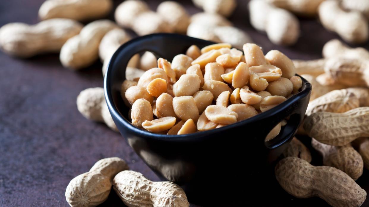  Close-up image of a navy-colored bowl containing salted peanuts with some unopened peanuts in their shells surrounding the bowl . 
