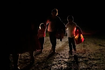 FILE PHOTO: A woman from Honduras and her two children are followed by a U.S. Border Patrol vehicle as they walk along a dirt road