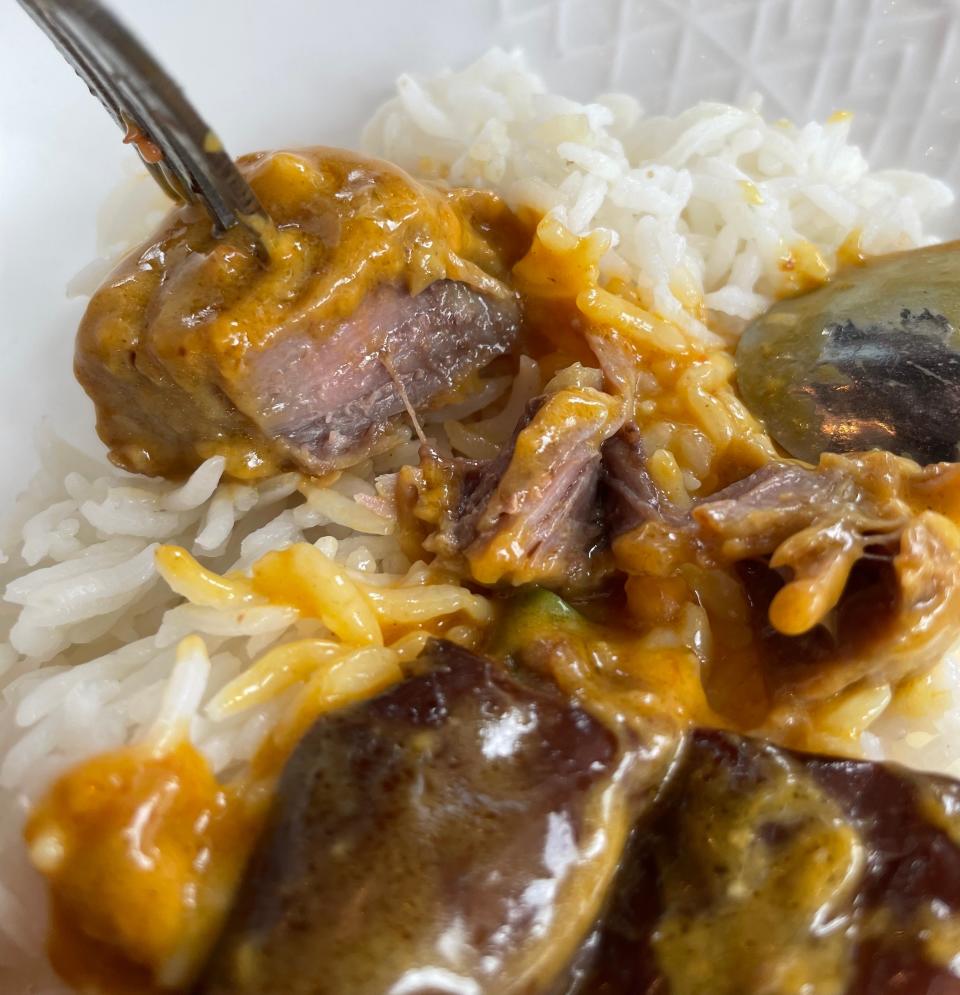 A fork is picking up a piece of braised meat over a plate of white rice with a rich, brown sauce