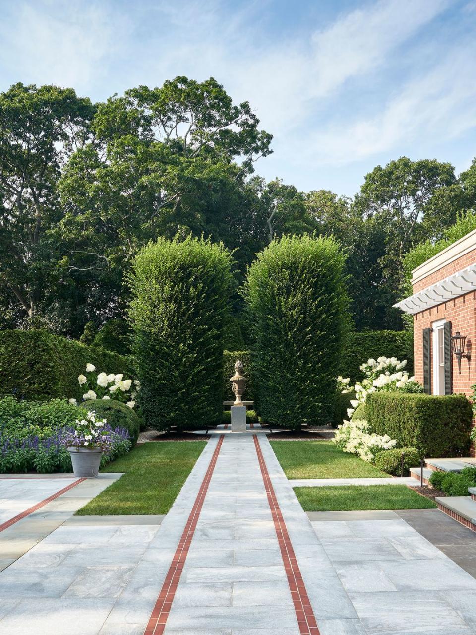 classic long paved walkway to a pedestal topped with an urn between two large pine trees
