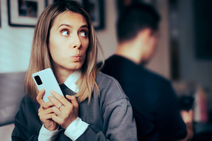 Woman holding a smartphone and looking suspiciously to the side while a man is turned away, engrossed in his own phone