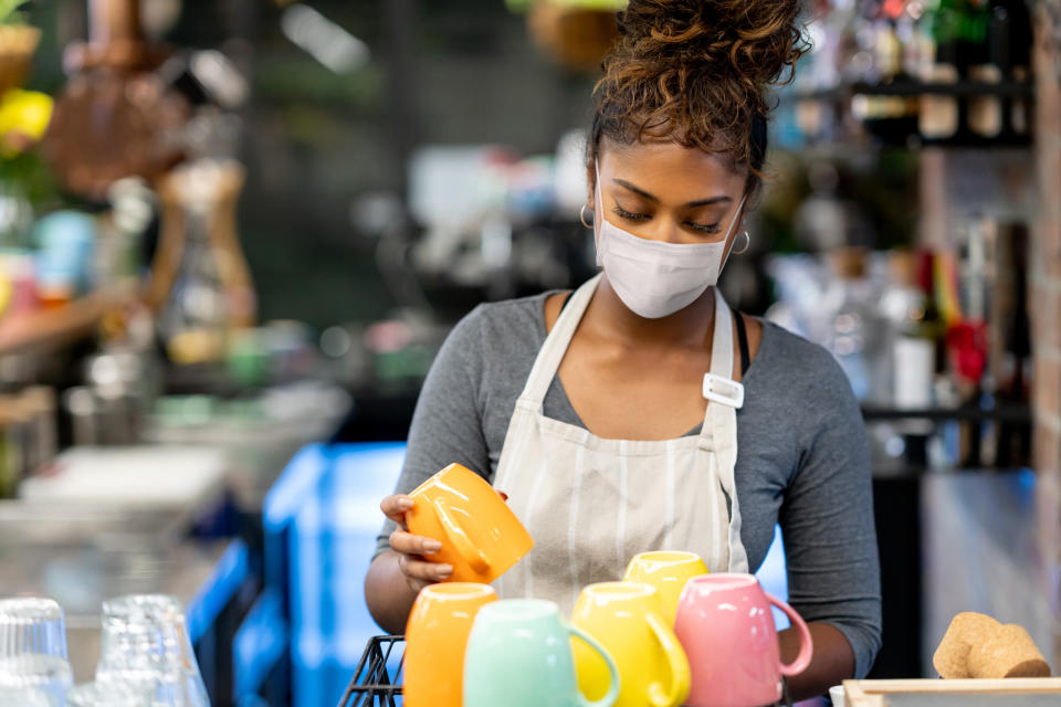 Waitress working at a cafe wearing a facemask while washing the dishes during the COVID-19 pandemic