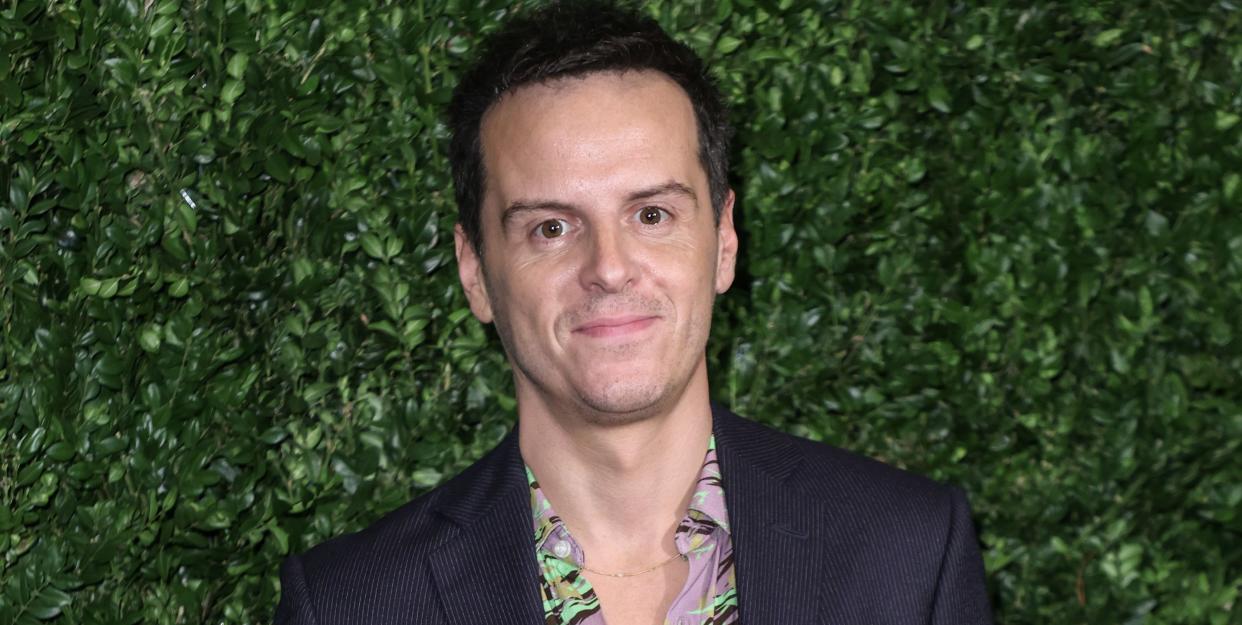 andrew scott, a man with short brown hair stands looking at the camera with a slight smile and right hand in his trouser pocket, he wears a pink shirt with black suit trousers and jacket