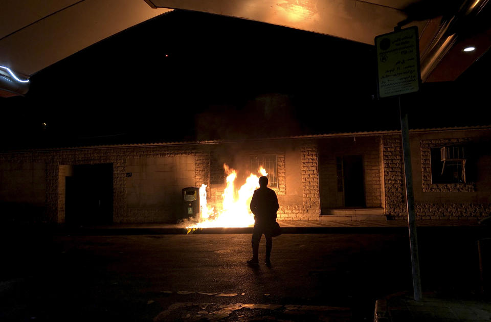 In this photograph taken Sunday, Jan. 12, 2020, a man stands in front of a fire set amid demonstrations in Tehran, Iran, to remember victims of a Ukrainian airplane shot down by an Iranian missile. Online videos purported to show Monday, Jan. 13, 2020, that Iranian security forces fired both live ammunition and tear gas to disperse demonstrators protesting against the Islamic Republic's initial denial that it shot down a Ukrainian jetliner. (AP Photo)