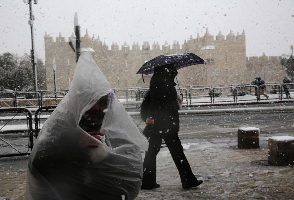 A man covers himself with a plastic bag near Damascus Gate outside Jerusalem's Old City during a snowstorm in winter December 12, 2013. REUTERS/Darren Whiteside (JERUSALEM - Tags: ENVIRONMENT)