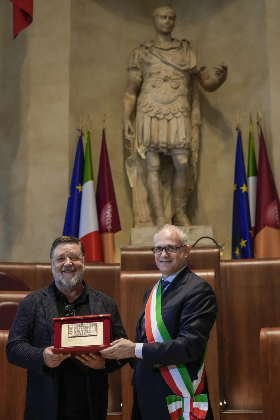 Actor Russel Crowe, left, poses under a statue of ancient Roman emperor Julius Cesar with the "Ambassador of Rome in the World" award he received from Rome's mayor Roberto Gualtieri, in Rome's Capitol Hill, Friday, Oct. 14, 2022. (AP Photo/Andrew Medichini)