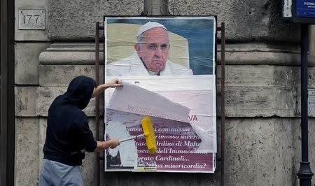 A worker covers with a banner reading "illegal poster" a poster depicting Pope Francis and accusing him of attacking conservative Catholics, in Rome, Italy, February 5, 2017. REUTERS/Max Rossi/File Photo