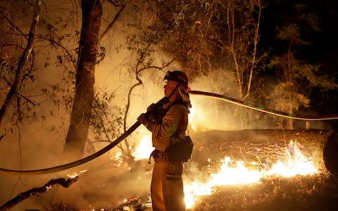 A firefighter holds a water hose while fighting a wildfire in Santa Rosa - Credit: AP