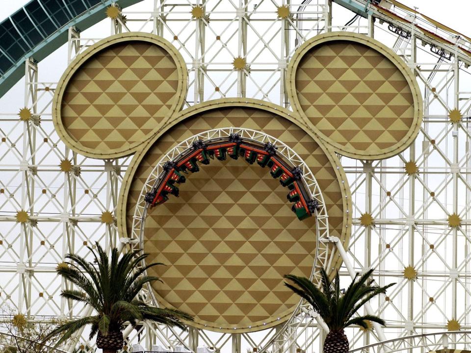 A rollercoaster with a giant Mickey Mouse head-shaped structure and tracks that loop in front of it. Cars and people are riding upside down in the loop.