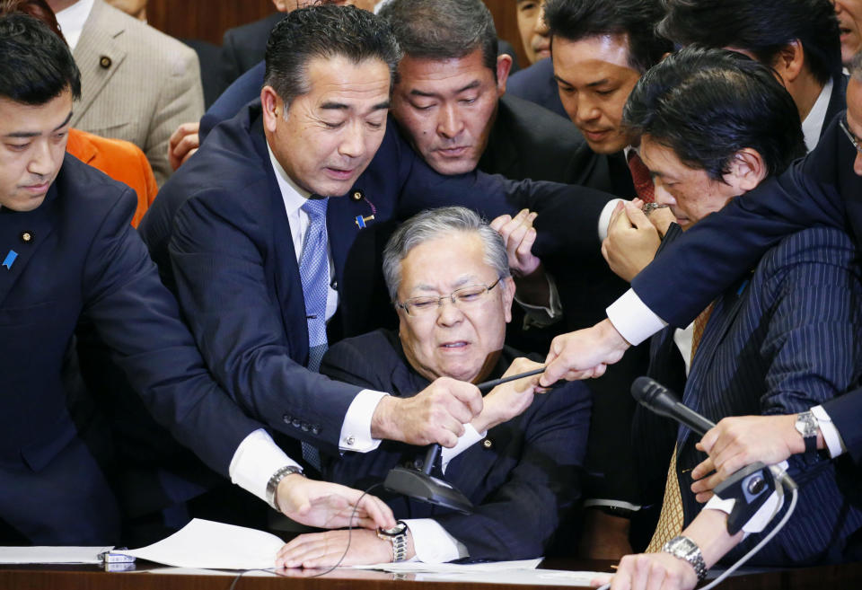 Japan's ruling parties and opposition parties' members scramble for a microphone as opposition parties try to stop Judicial Affairs Committee Chairman Shinichi Yokoyama, bottom center, from moving to hold a vote for a bill to revise an immigration control law, at upper house committee in Tokyo early Saturday, Dec. 8, 2018. Japan is preparing to officially open the door to foreign workers to do unskilled jobs and possibly eventually become citizens. (Toshiyuki Matsumoto/Kyodo News via AP)