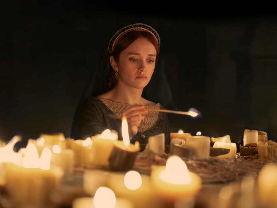 olivia cooke as alicent hightower, lighting candles while wearing a green dress.