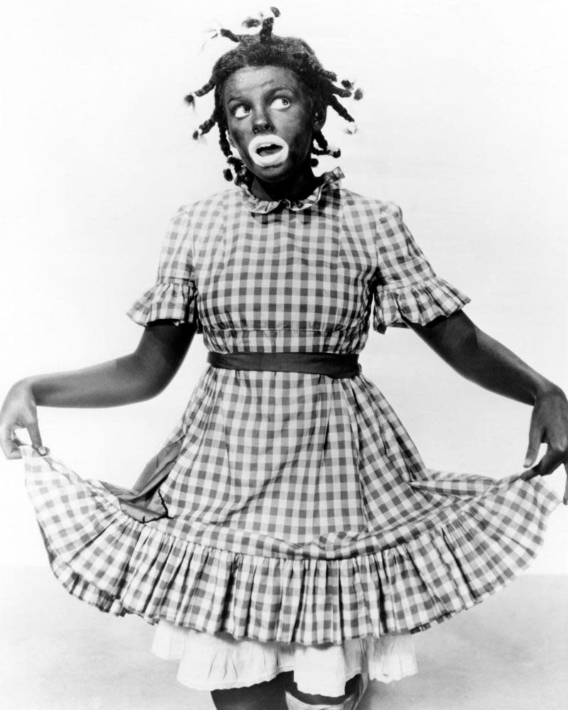 Judy Garland, in blackface and her hair braided, holding up the hem of her gingham dress in Everybody Sing (1938)