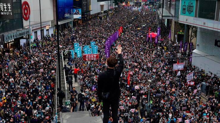 01.01.2020, China, Hongkong: Ein Demonstrant steht während eines großen pro-demokratischen Protestmarsches erhöht zu einer Straße, auf der zahlreiche Menschen entlanggehen, und hält eine Hand in die Höhe, um die fünf Forderungen der Demonstranten an die Regierung zu symbolisieren. Wegen der anhaltenden Proteste hat Hongkong dieses Silvester ohne Feuerwerk-Spektakel gefeiert. Foto: Vincent Yu/AP/dpa +++ dpa-Bildfunk +++ Foto: dpa