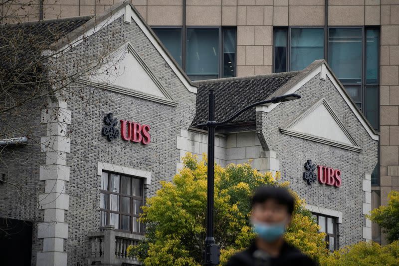 A person stands in front of the logo of Swiss bank UBS, seen at the bank's branch in Shanghai