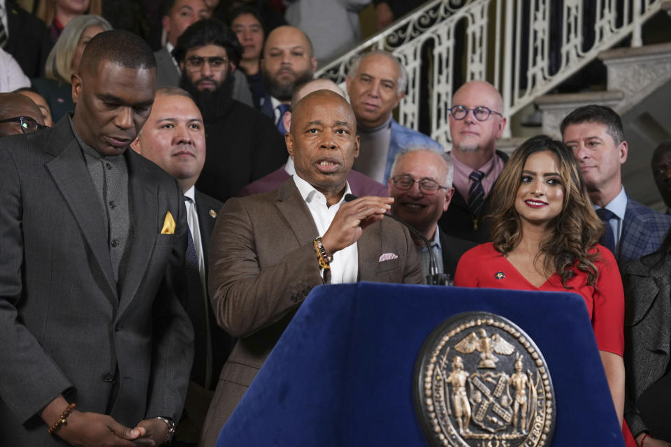 New York City mayor Eric Adams, at a podium with the New York City seal, is surrounded by dozens of officials.