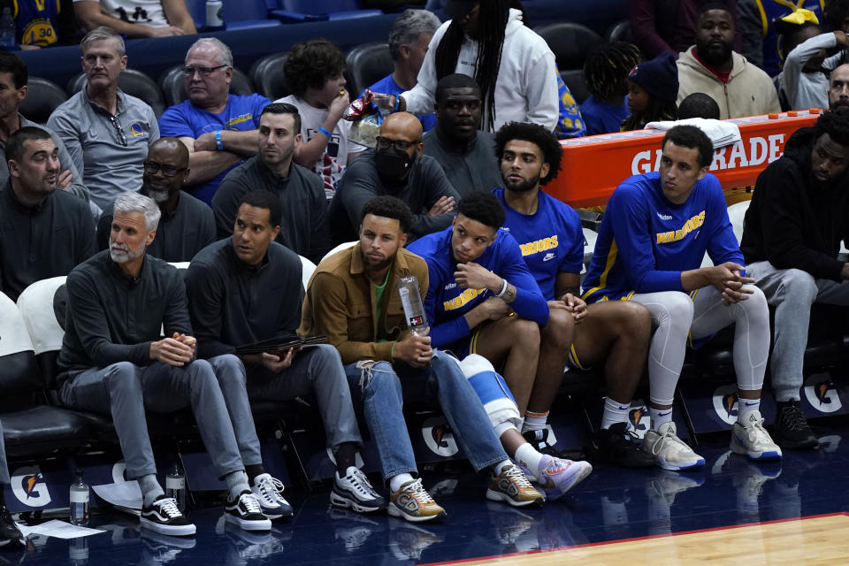 Golden State Warriors guard Stephen Curry, center, sits on the bench in street clothes in the second half of an NBA basketball game against the Golden State Warriors in New Orleans, Monday, Nov. 21, 2022. The Pelicans won 128-83. (AP Photo/Gerald Herbert)