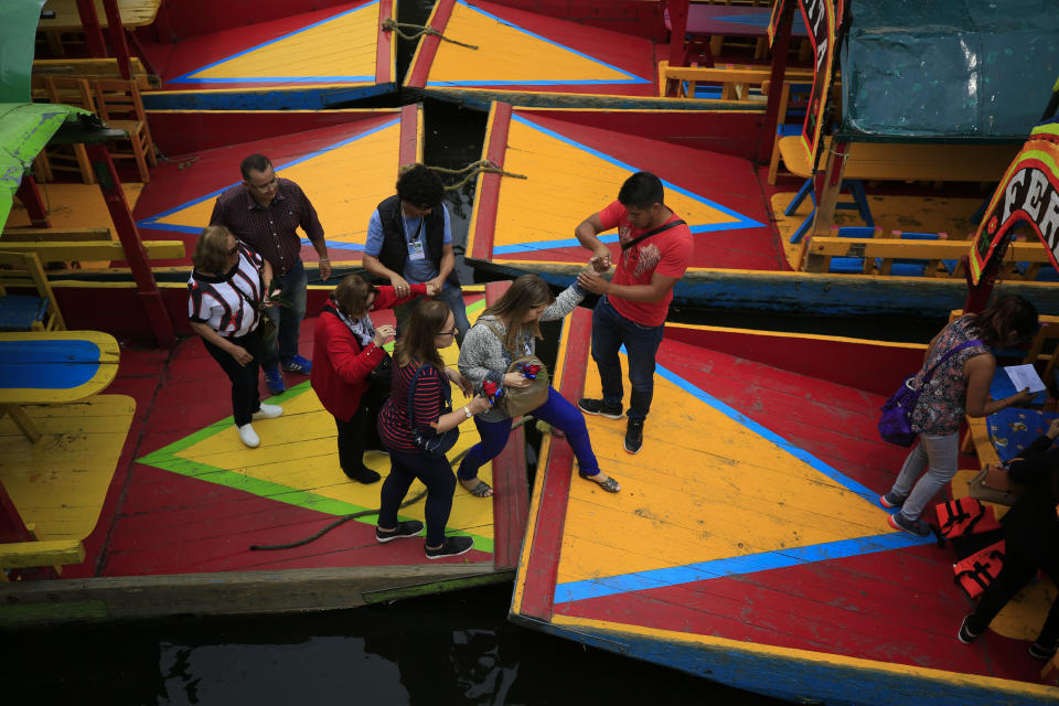 Passengers are helped to step between trajineras, colorful passenger boats typically rented by tourists, families, and groups of young people, as they board a boat in Xochimilco, Mexico City, Friday, Sept. 6, 2019. The usually festive Nativitas pier was subdued and largely empty Friday afternoon, with some boat operators and vendors estimating that business was down by 80% on the first weekend following the drowning death of a youth that was captured on cellphone video and seen widely in Mexico. Borough officials stood on the pier to inform visitors of new regulations that went into effect Friday limiting the consumption of alcohol, prohibiting the use of speakers and instructing visitors to remain seated.(AP Photo/Rebecca Blackwell)