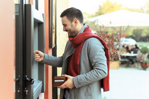 A person in a coat and red scarf smiling while using an ATM.