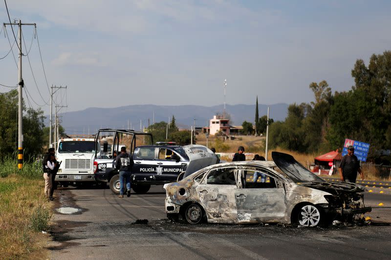 Police stand near the wreckage of a car that was burnt in a blockade set by members of the Santa Rosa de Lima Cartel to repel security forces during a police operation on the outskirts of Celaya