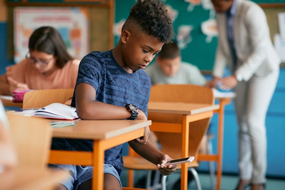 A sitting at a desk in a classroom looking at a smartphone