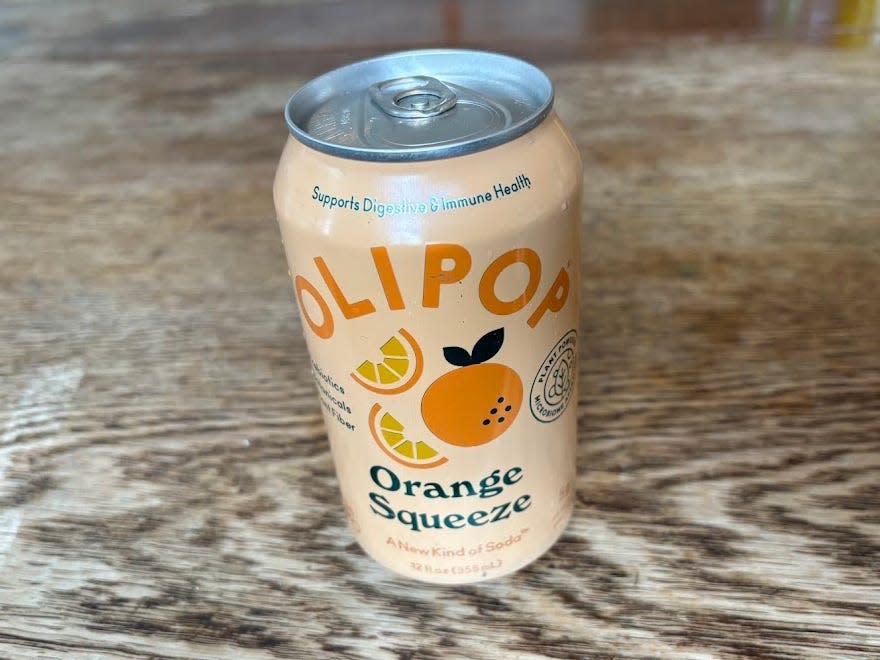 A can of orange squeeze Olipop on a wooden table.
