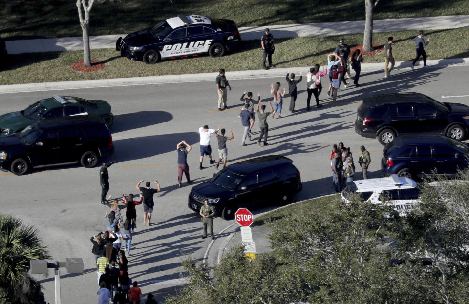 Estudiantes de la escuela Stoneman Douglas High, en Parkland, Florida, al ser evacuados por la policía tras el tiroteo que dejó allí 17 muertos a manos de un exalumno del plantel. (AP)