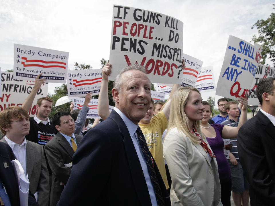 Rich Heller is surrounded by activists holding signs aloft reading: If guns kill people, do pens misspell words? and Brady Campaign, to prevent gun violence.