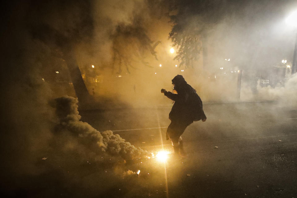 FILE - In this July 29, 2020, file photo, a demonstrator kicks a tear gas canister back at federal officers during a Black Lives Matter protest at the Mark O. Hatfield U.S. Courthouse in Portland, Ore. Interviews by The Associated Press with medical researchers, federal regulatory agencies, and a review of U.S. government-funded scientific studies raise questions about the safety of the gas, especially its use on individuals in confined spaces, in excessive quantities, and when it’s fired directly at protesters. (AP Photo/Marcio Jose Sanchez, File)