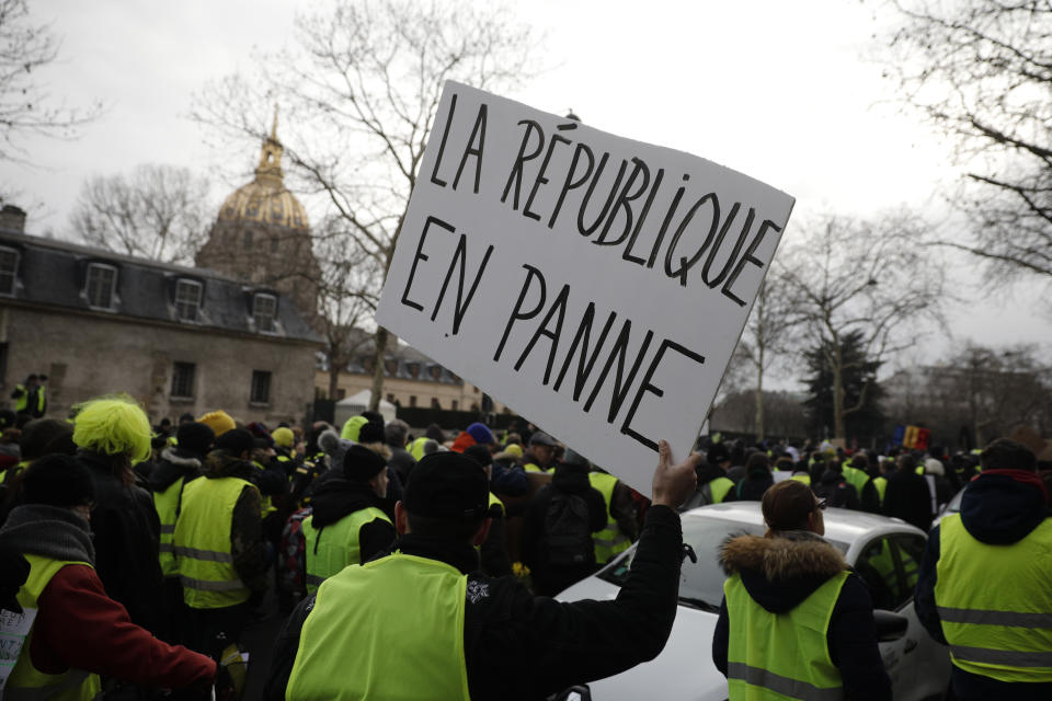 Yellow vest demonstrators, one carrying a poster reading "Republic Broken", march in Paris, Saturday, Jan.19, 2019. Yellow vest protesters are planning rallies in several French cities despite a national debate launched this week by President Emmanuel Macron aimed at assuaging their anger. (AP Photo/Kamil Zihnioglu)