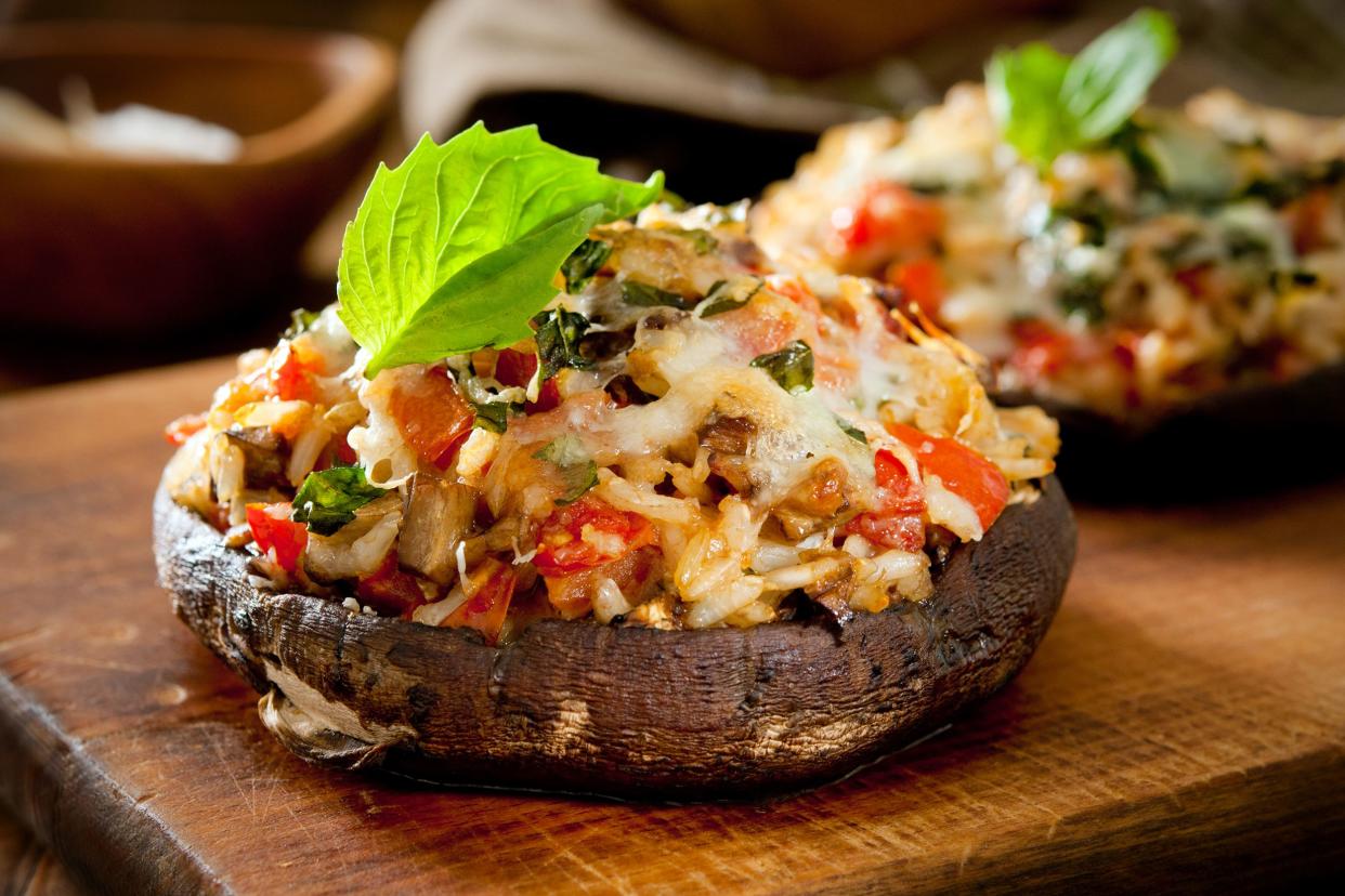 Two stuffed portobello mushrooms on a wooden cutting board