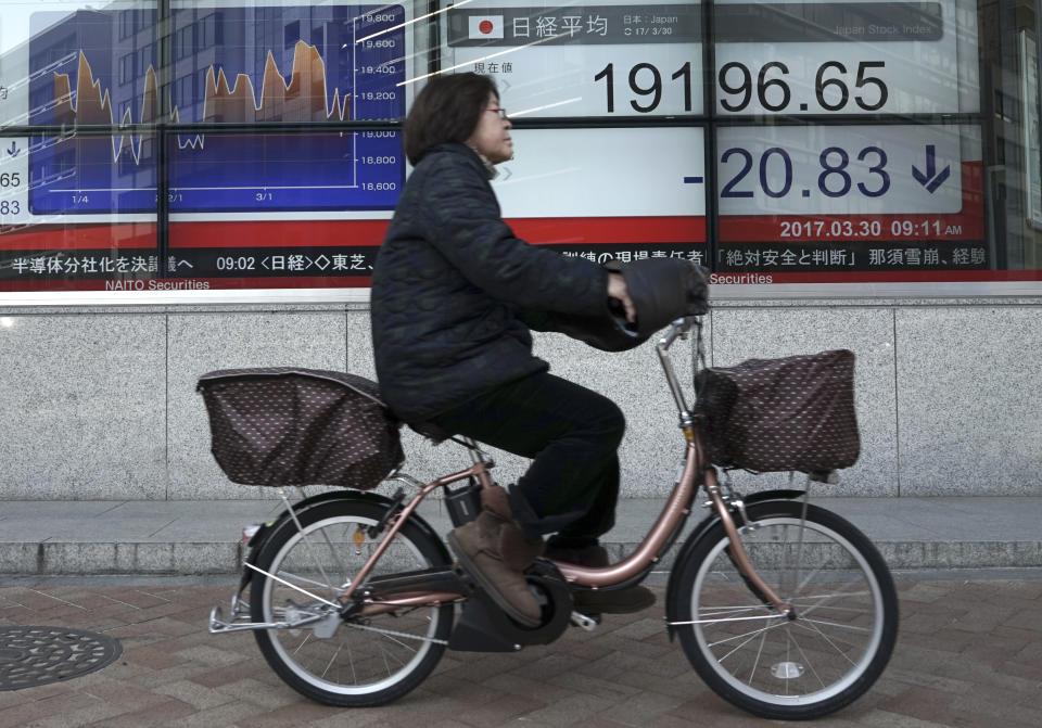 A woman rides a bicycle past an electronic stock board showing Japan's Nikkei 225 index at a securities firm in Tokyo, Thursday, March 30, 2017. Asian stocks are drifting lower on Thursday after a lackluster performance on Wall Street. (AP Photo/Eugene Hoshiko)