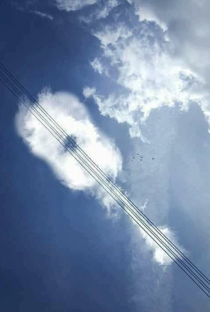 cloud shaped like a guitar hanging above electric lines to make it seem like those are the strings