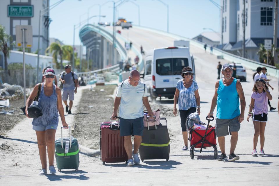 Fort Myers Beach residents walk northbound on San Carlos Boulevard after retrieving belongings from home and descending the bridge over Matanzas Harbor after Hurricane Ian passed through the region Wednesday afternoon in Fort Myers, FL., on Friday, September 30, 2022.