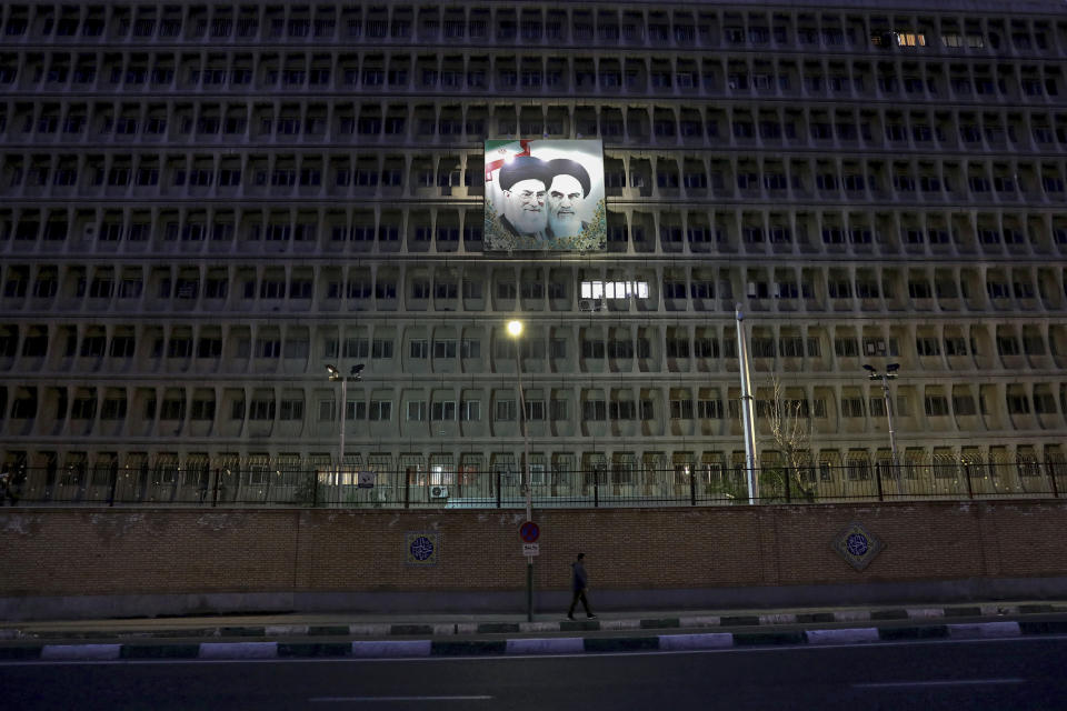 In this Tuesday, March 24, 2020 photo, a pedestrian walks past an army garrison adorned with portraits of the late Iranian revolutionary founder Ayatollah Khomeini, top right, and Supreme Leader Ayatollah Ali Khamenei, in Tehran, Iran. Due to the coronavirus outbreak and the COVID-19 illness it causes, life has changed dramatically on Tehran's main highways, in the narrow corridors of its historical Grand Bazaar and in the public spaces under portraits of its leaders. (AP Photo/Ebrahim Noroozi)