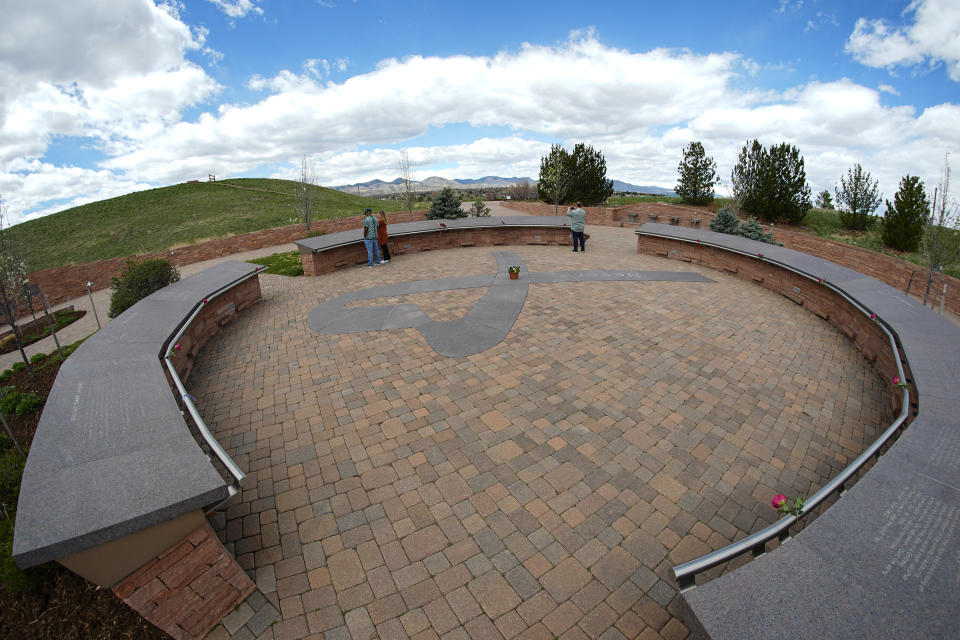 In this view through a fisheye lens, people visit the Columbine Memorial, Wednesday, April 17, 2024, in Littleton, Colo. Trauma still shadows the survivors of the horrific Columbine High School shooting as the attack's 25th anniversary approaches. (AP Photo/David Zalubowski)