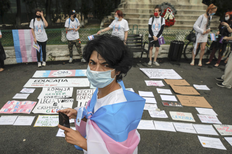 A protester, wearing a protective mask, takes photos of banners outside the presidential palace in Bucharest, Romania, Thursday, June 18, 2020, during a rally against a law banning the teaching of gender studies. Dozens of protesters gathered outside Bucharest's Cotroceni Presidential Palace, to express their opposition to a law banning the teaching of gender studies in the country's schools and universities and call on President Klaus Iohannis to reject signing the bill and send it back to parliament. (AP Photo/Vadim Ghirda)