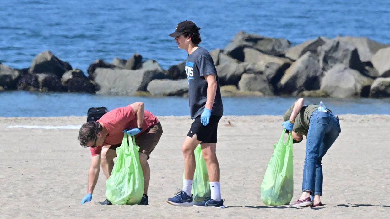 Three people are seen helping pick up trash at Venice Beach for Earth Day, 2023.