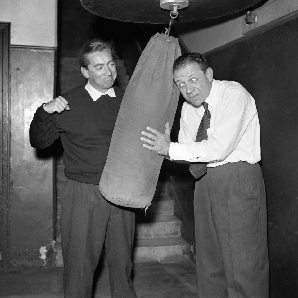 Comedian Tony Hancock (left) limbers up with a punchbag, assisted by a somewhat apprehensive Sidney James.
There's no fight ahead of Hancock, who is just in training for the television version of his 'Half Hour' which is being screened fortnightly by the BBC.