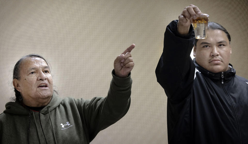 Joe Lafferty, of Iron Lightning, S.D., points to a glass with a mixture of water and oil held by Oscar High Elk, of Green Grass, S.D., while suggesting that those behind the Dakota Access Pipeline drink from the cup during a U.S. Army Corps of Engineers public meeting on DAPL at The Radisson Hotel in Bismarck, N.D., on Wednesday, Nov. 1, 2023. (Darren Gibbins/The Bismarck Tribune via AP)