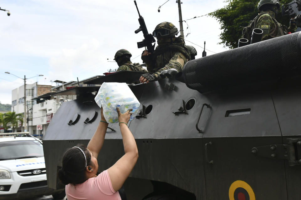 Una mujer regala un pack de botellas de agua a militares que patrullan en vehículos blindados por las calles, en Portoviejo, Ecuador, el jueves 11 de enero de 2024. El presidente Daniel Noboa decretó el lunes un estado de excepción nacional que suspende derechos ciudadanos y permite movilizar al Ejército en tareas de seguridad, ante la última secuencia de ataques violentos en el país. (AP Foto/Ariel Ochoa)