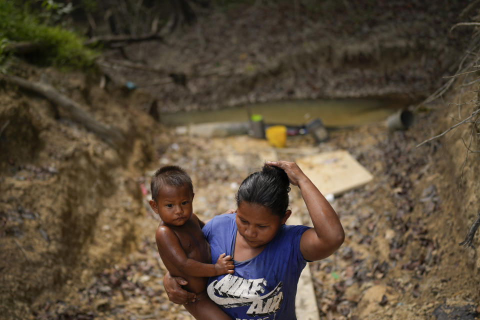 An Amerindian woman carries her child after bathing him in a river, in Chinese Landing, Guyana, Monday, April 17, 2023. Descendants of Caribs, the Amerindians living in Chinese Landing have seen their land shrink as miners scrape back layers of rock and red soil. (AP Photo/Matias Delacroix)