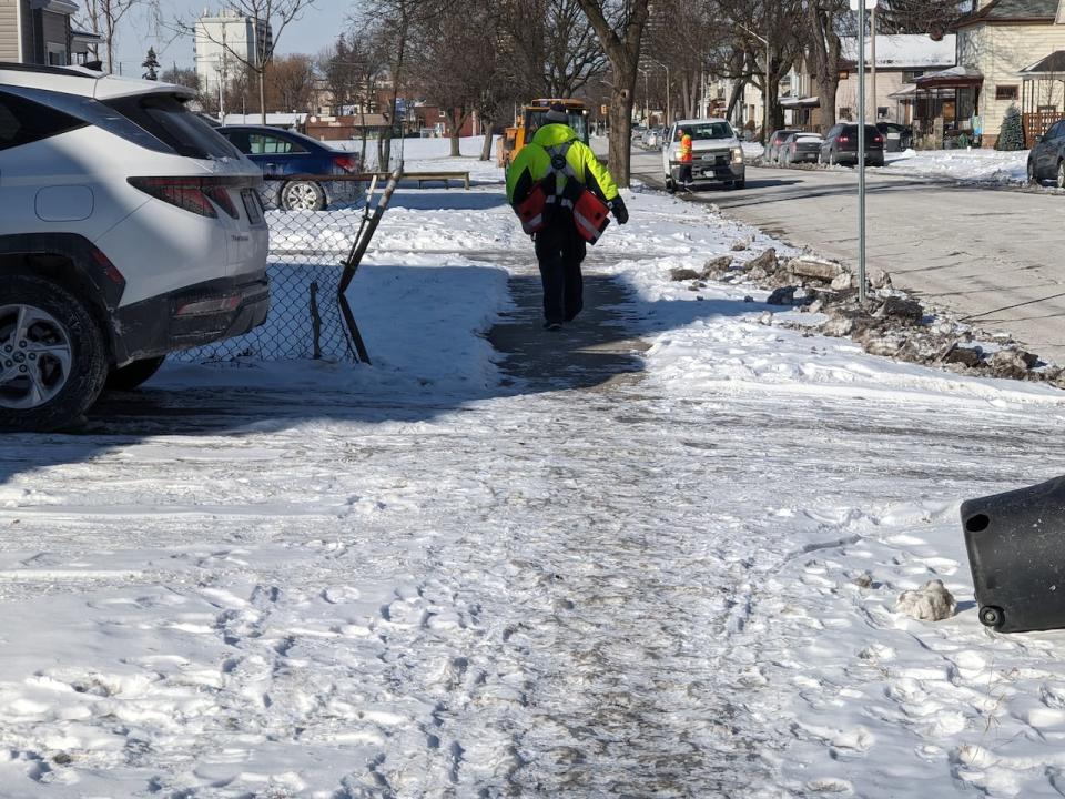 A Canada Post mail carrier walks along a sidewalk in Windsor on Wednesday, Jan. 17, 2024. The City of Windsor reminds residents its their responsibility to clear sidewalks — but says in cases where the snow has frozen, they just encourage effort in the way of salt or sand. 