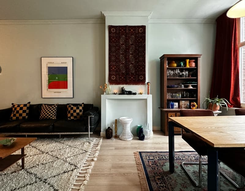 Living room and dining room with black leather vintage sofa, vintage rugs, and vintage art on the walls