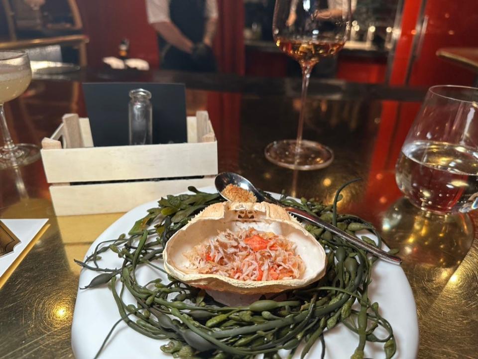 a shell filled with crab on top of a bed of seaweed-like vines at a restaurant