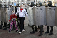 A woman with her child walks through a police line blocking the road to prevent against an opposition rally to protest the official presidential election results in Minsk, Belarus, Sunday, Sept. 20, 2020. Tens of thousands of Belarusians calling for the authoritarian president to resign marched through the capital on Sunday as the country's wave of protests entered its seventh week. Hundreds of soldiers blocked off the center of Minsk, deploying water cannon and armored personnel carriers and erecting barbed wire barriers. (AP Photo/TUT.by)