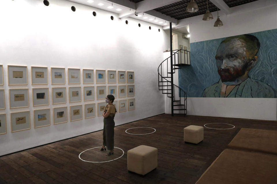 A visitor looks at art pieces by Indonesian artist Hanafi as she stands on a physical distancing marker placed on the floor as a precaution against the new coronavirus during an exhibition at Kertas Gallery in di Depok, West Java, Indonesia, Thursday, July 9, 2020. (AP Photo/Tatan Syuflana)