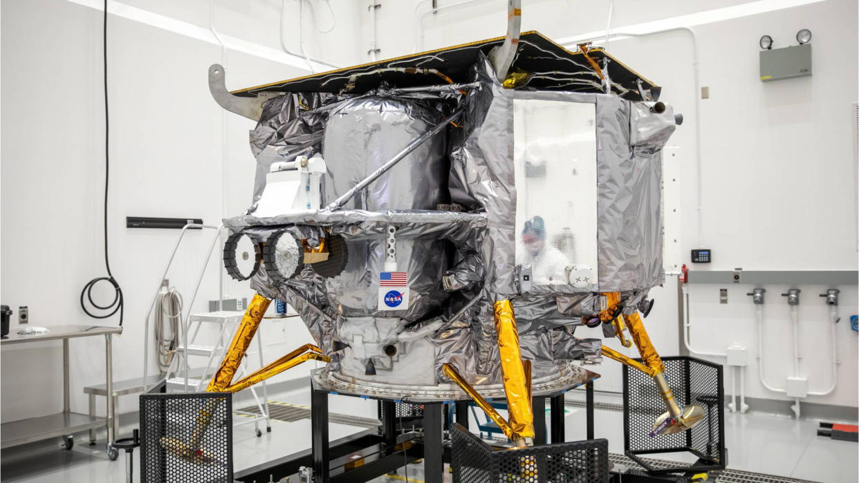  A silver spacecraft with gold legs sits in a white room. 