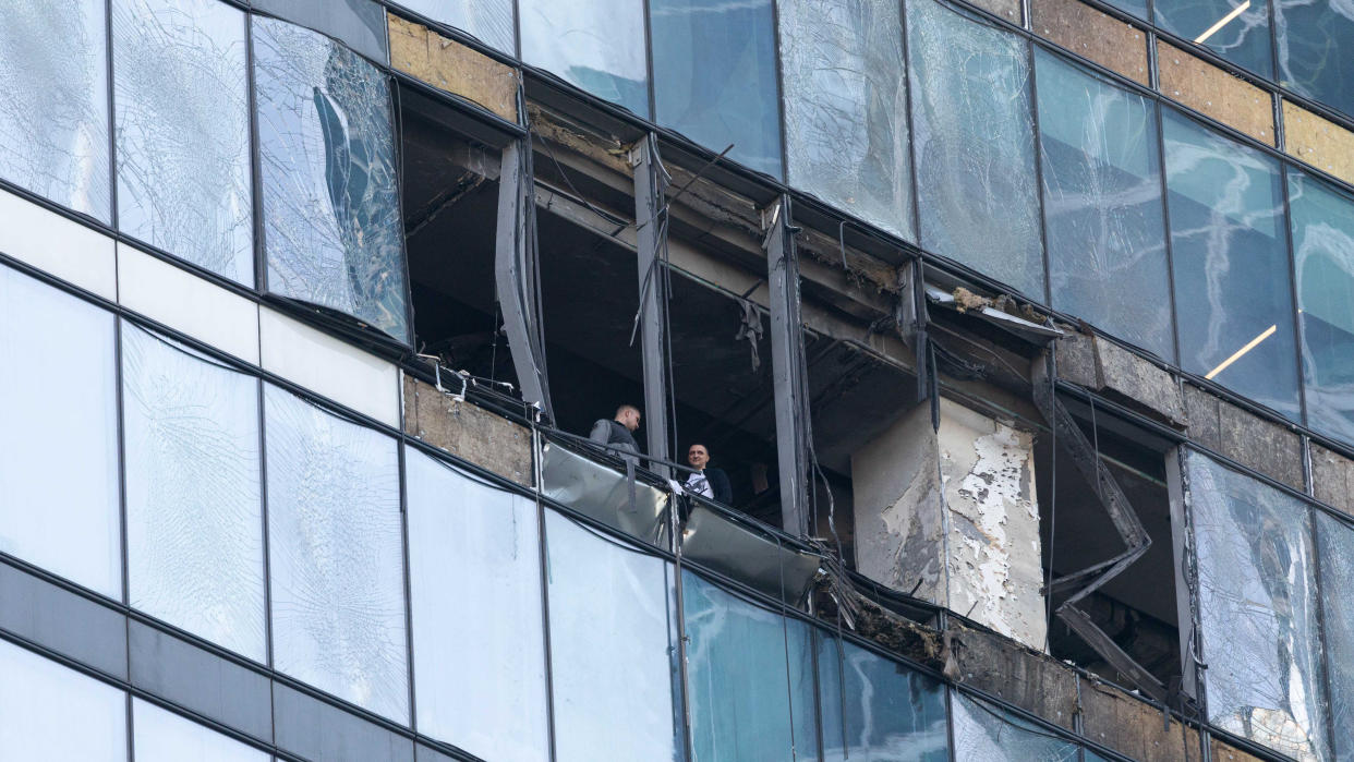 Two men stand in the burned-out, broken windows of a building.